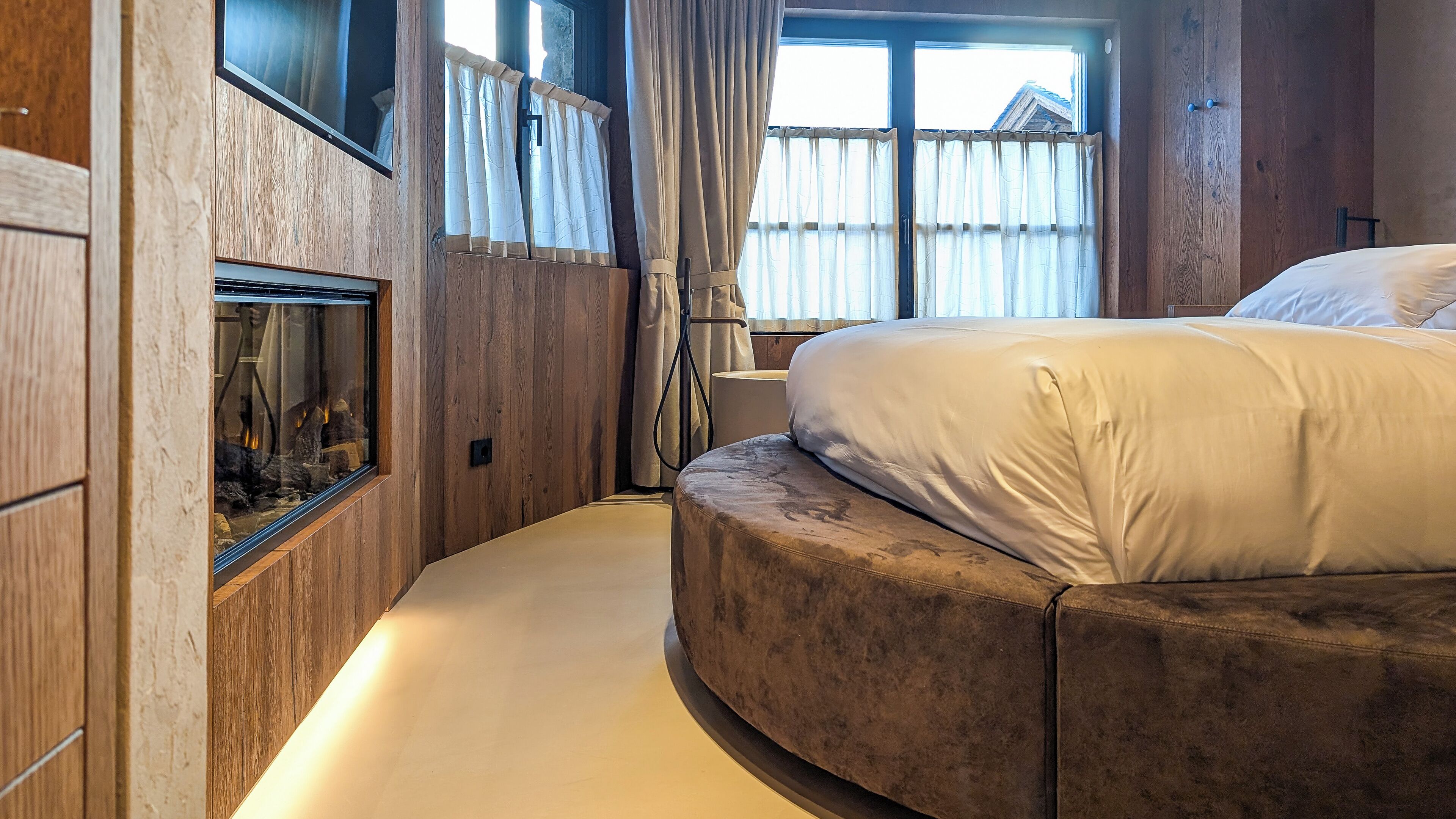 Une chambre avec un grand lit, des murs en bois, une cheminée et une fenêtre avec des rideaux.