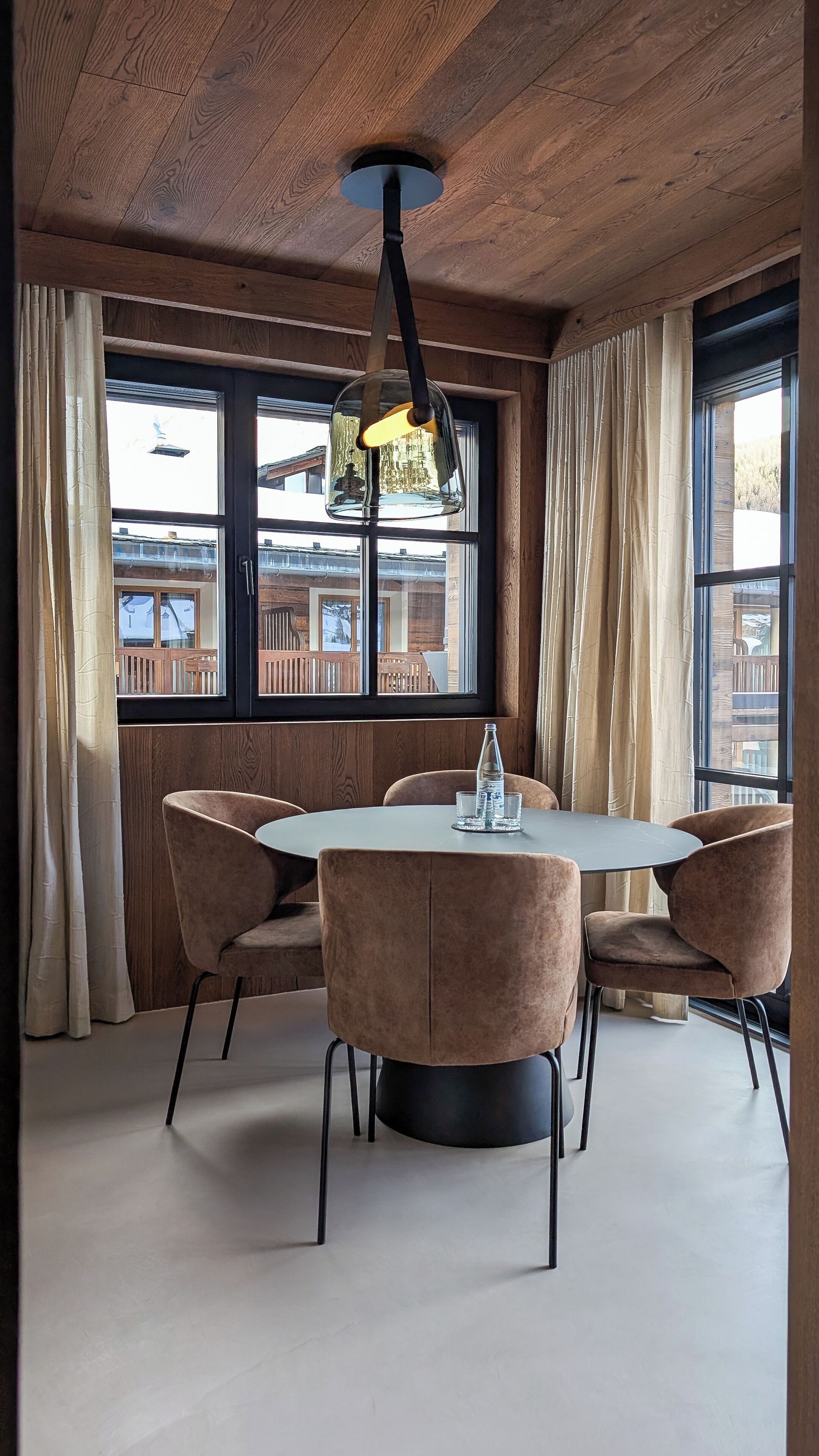A dining area with a round table, four chairs, and a hanging light fixture.