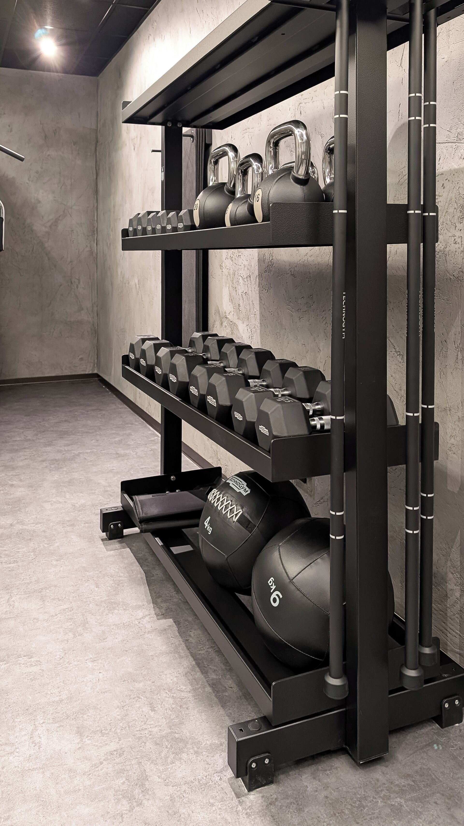 A gym with weightlifting equipment, including dumbbells and kettlebells, on racks.