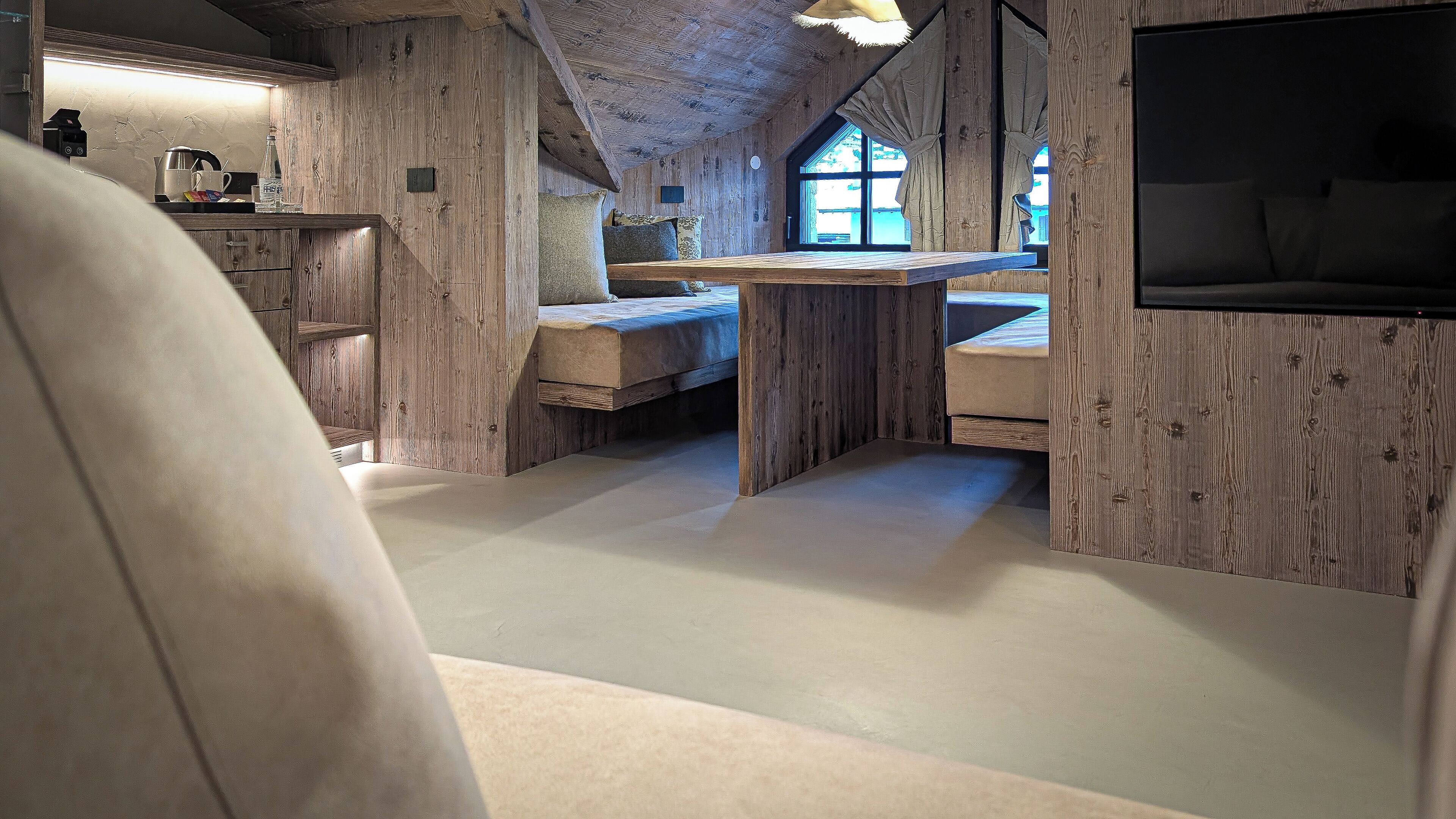 A rustic interior with wooden walls, a loft bed, a small table, and a TV mounted on the wall.