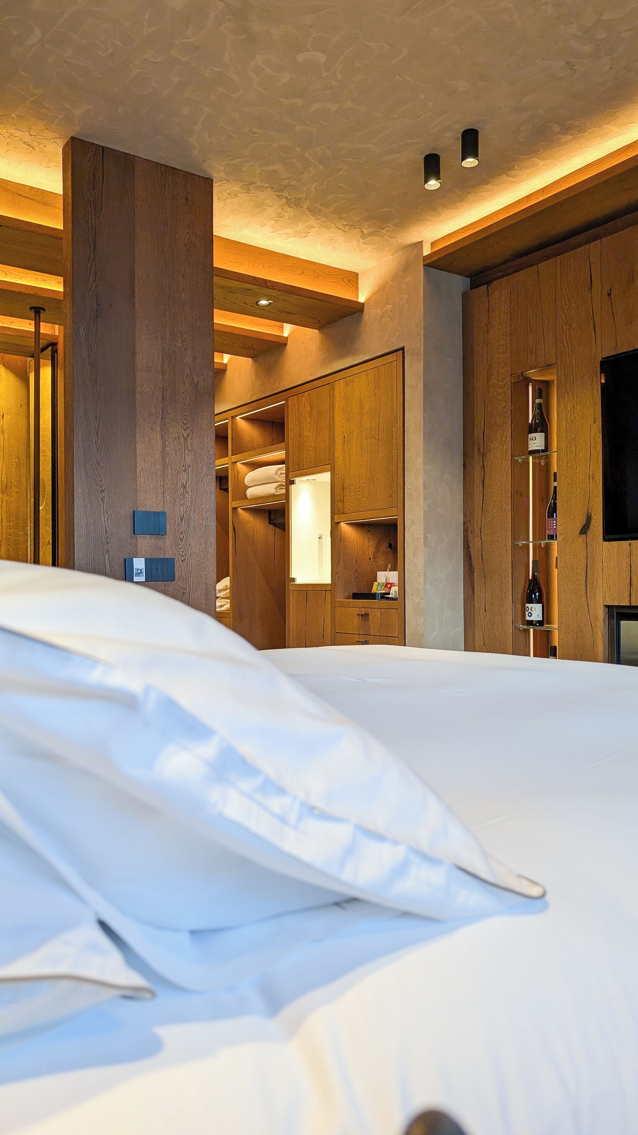 A hotel room with a large bed, wooden paneling, a built-in wardrobe, and a wine rack.