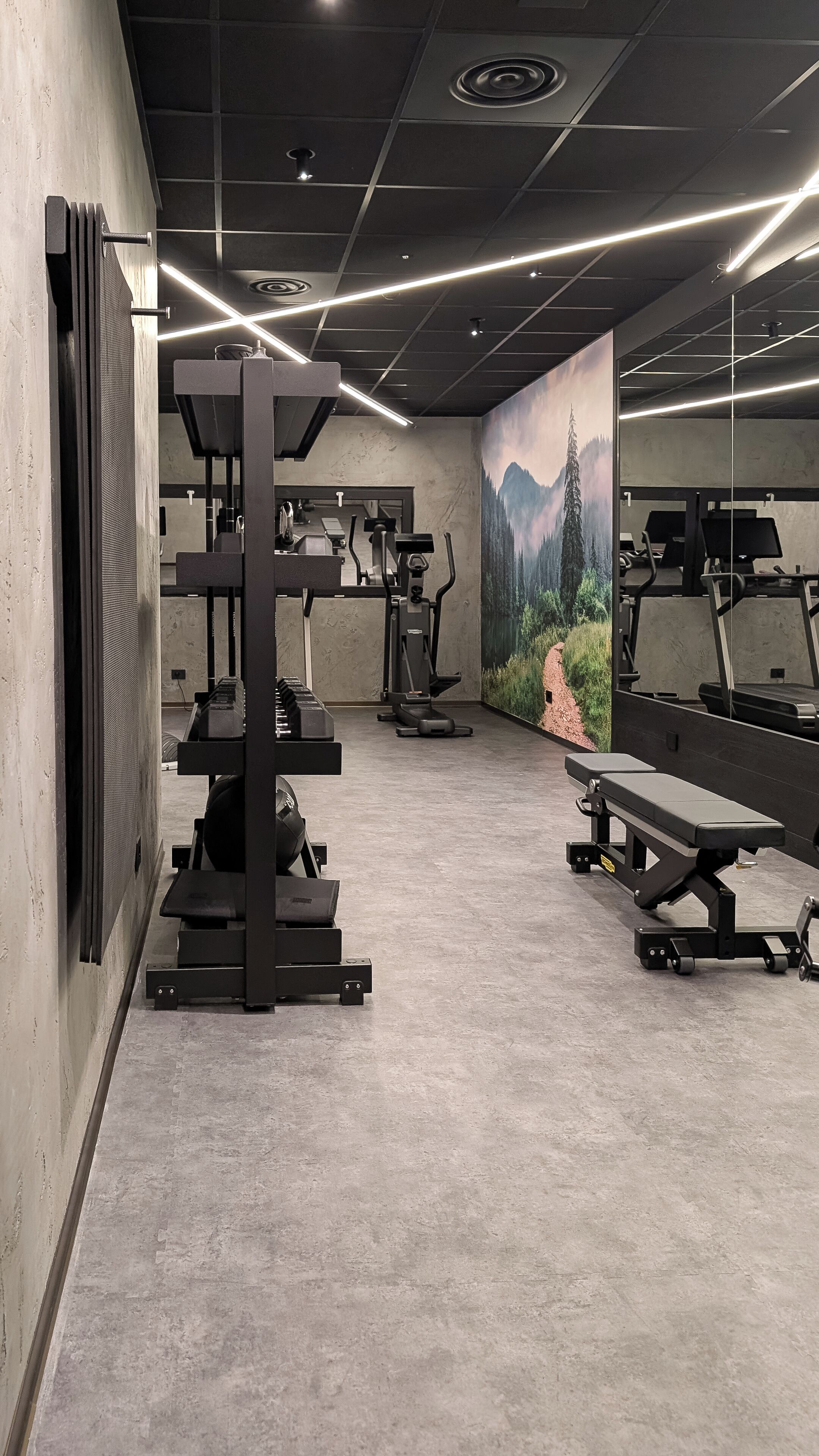 A gym with exercise equipment, a mural, and a concrete floor.