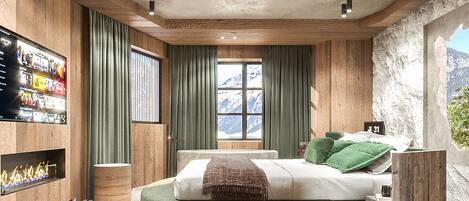Un dormitorio moderno con una cama redonda, paredes de madera, un ventanal grande y un televisor en la pared izquierda.