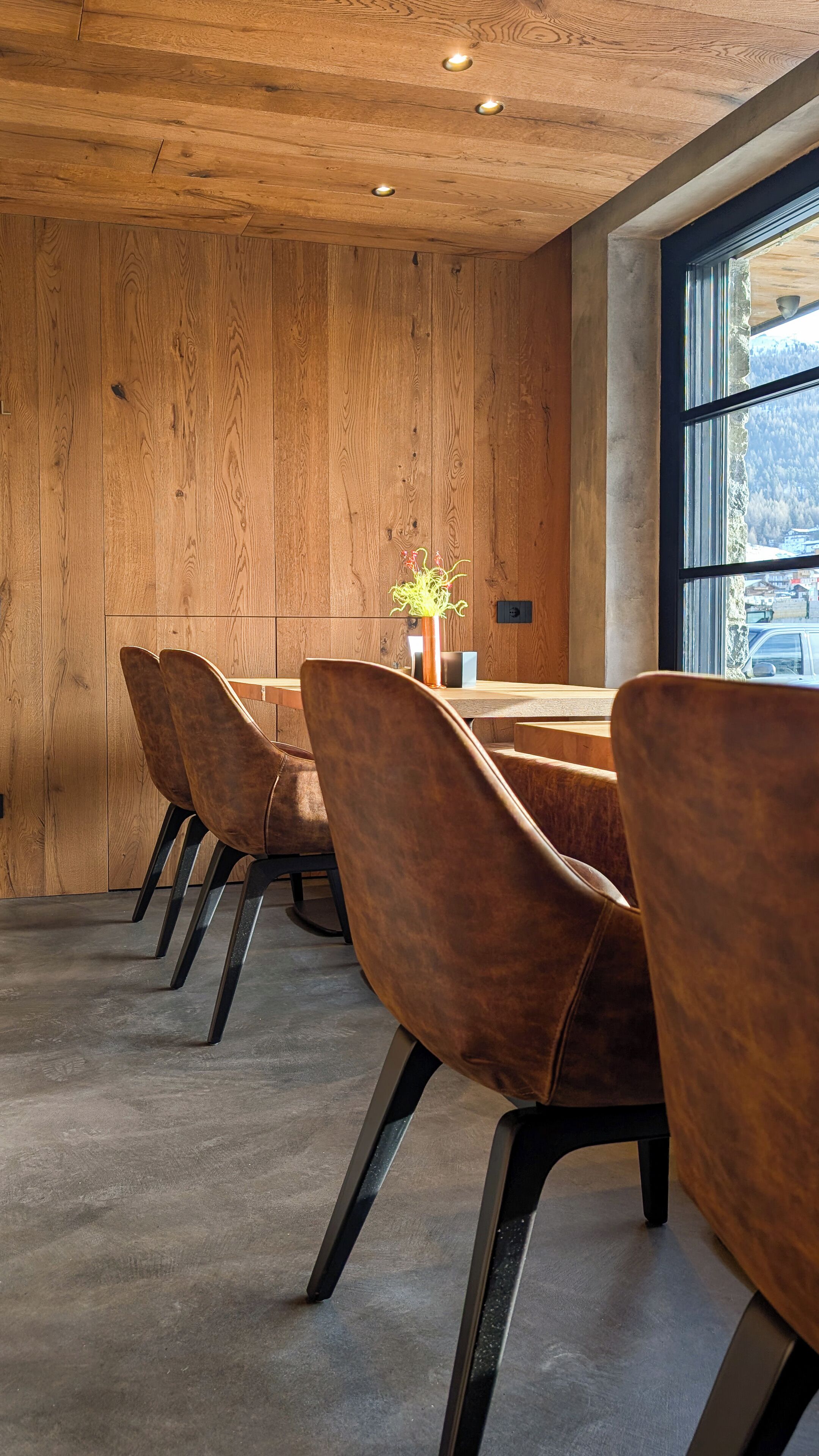 A modern dining area with wooden walls, a large window, and a table with chairs.