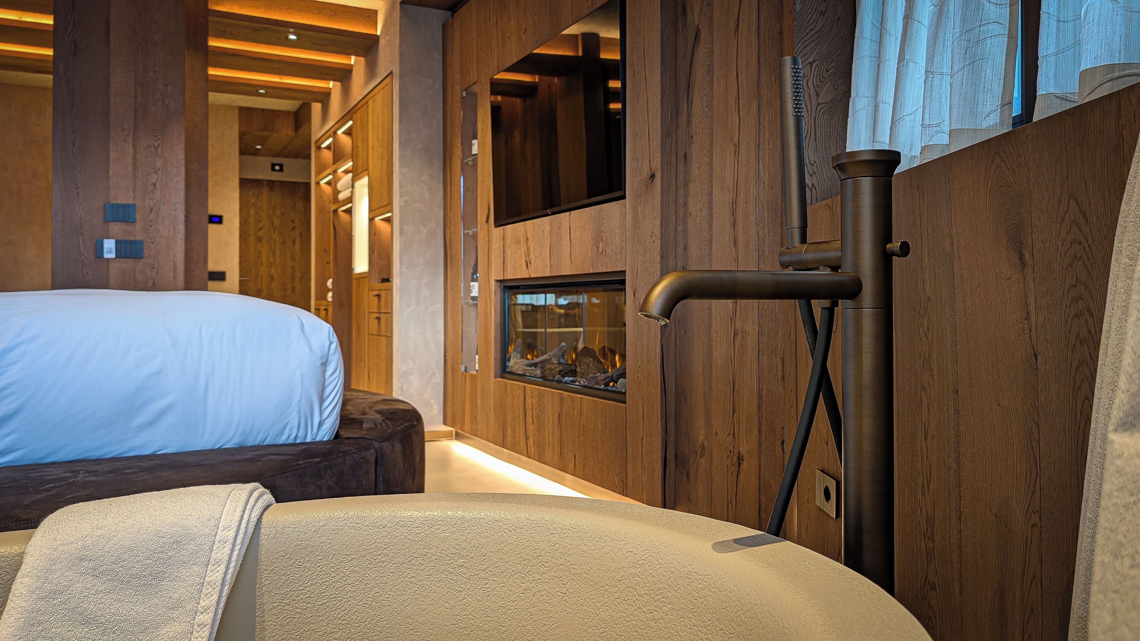 Una habitación de hotel moderna con una cama grande, chimenea empotrada y paneles de madera.