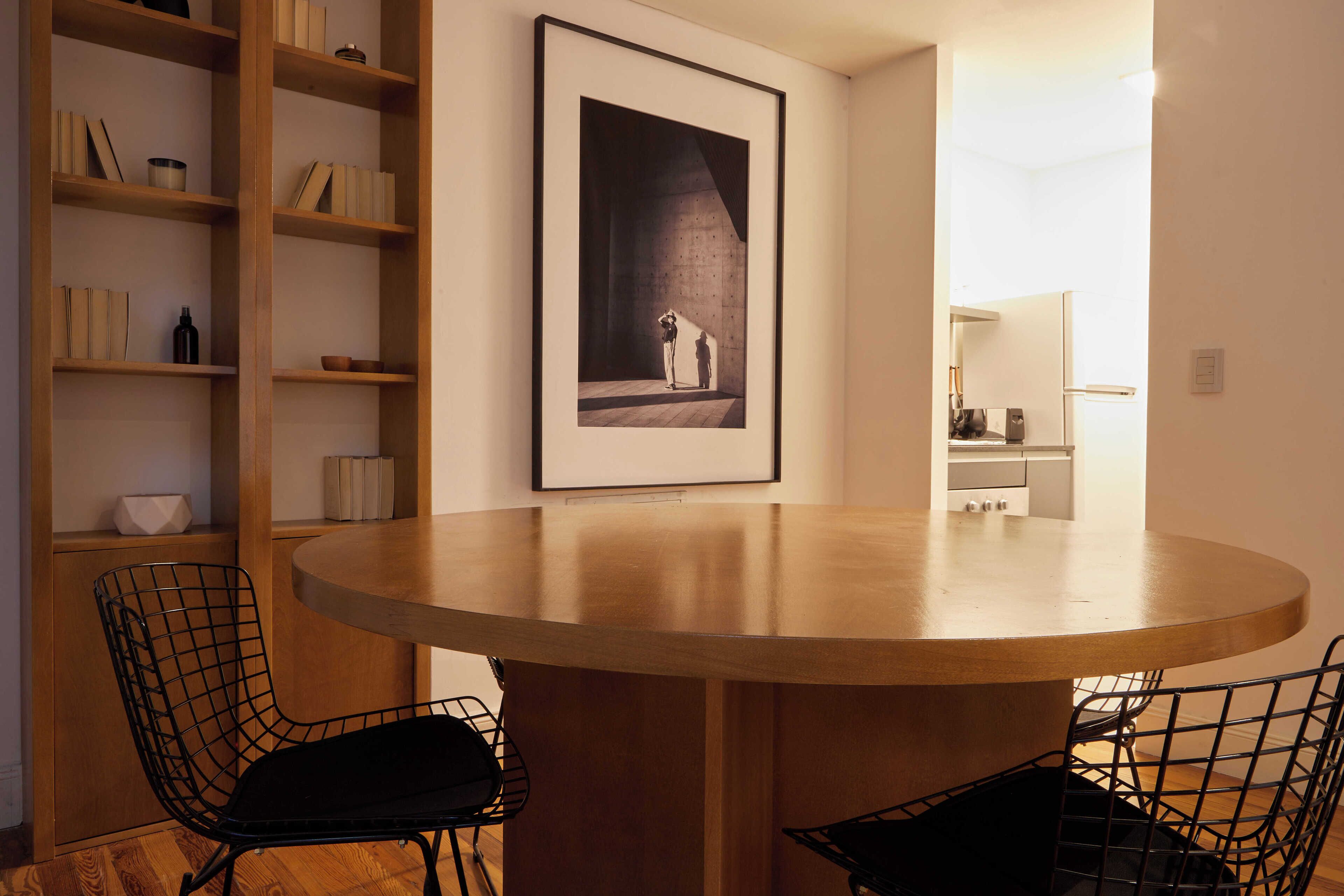 A modern dining area with a round wooden table, black wire chairs, and a bookshelf with books and decorative items.