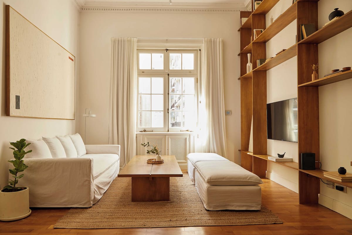 A modern living room with a sofa, ottoman, coffee table, and wooden shelving.