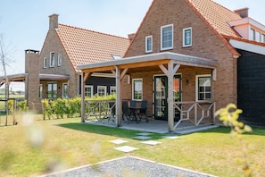Une maison en briques avec un patio couvert, un jardin et un ciel dégagé.