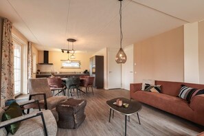 Un salon moderne avec un canapé, des fauteuils, une table basse et une cuisine en arrière-plan.