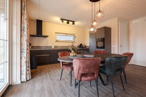 A modern kitchen with a dining area, featuring a round table, velvet chairs, and pendant lighting.