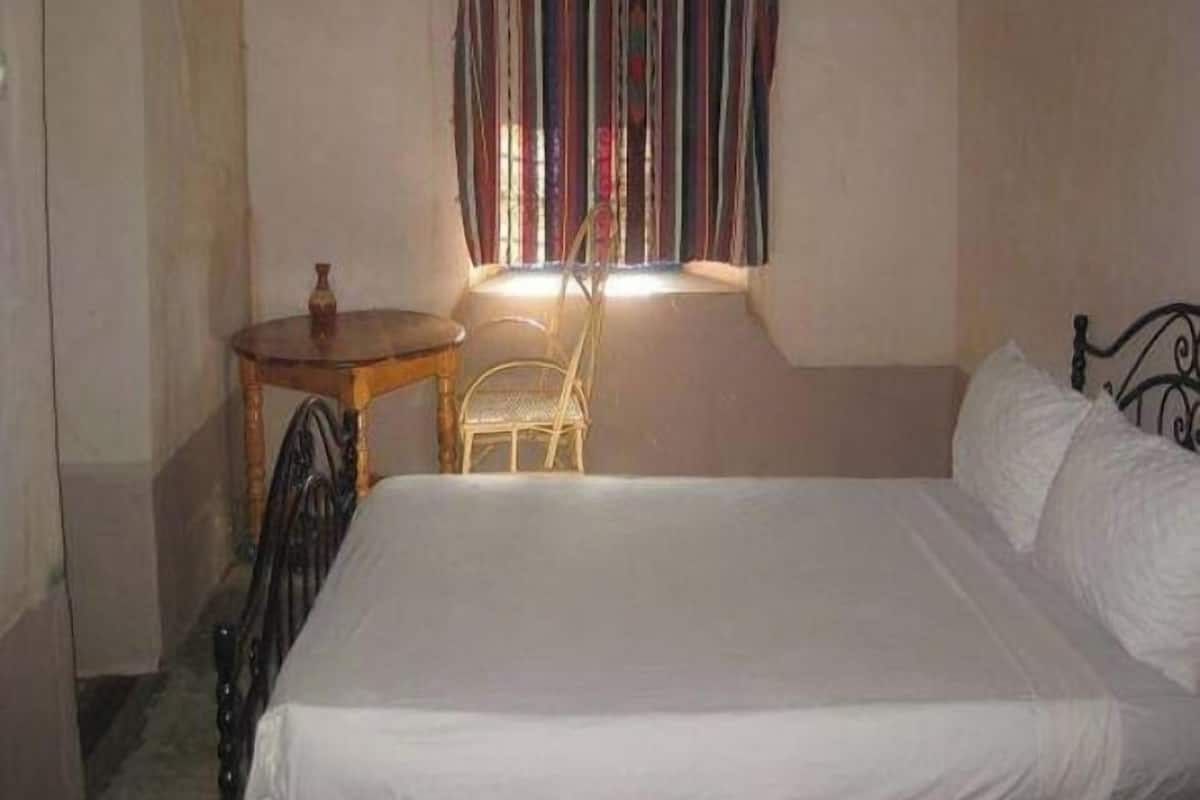 A bedroom with a bed, a small wooden table, a chair, and a window with striped curtains.