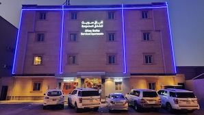 A building with multiple floors, a reception area, and several parked cars in front. - Afaq Suite Al- Shamisi - افاق سويت الشميسى (Riyadh)