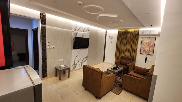 A modern living room with a sofa set, a coffee table, a flat-screen TV mounted on the wall, and a small side table with a phone. - Afaq Suite Al- Shamisi - افاق سويت الشميسى (Riyadh)
