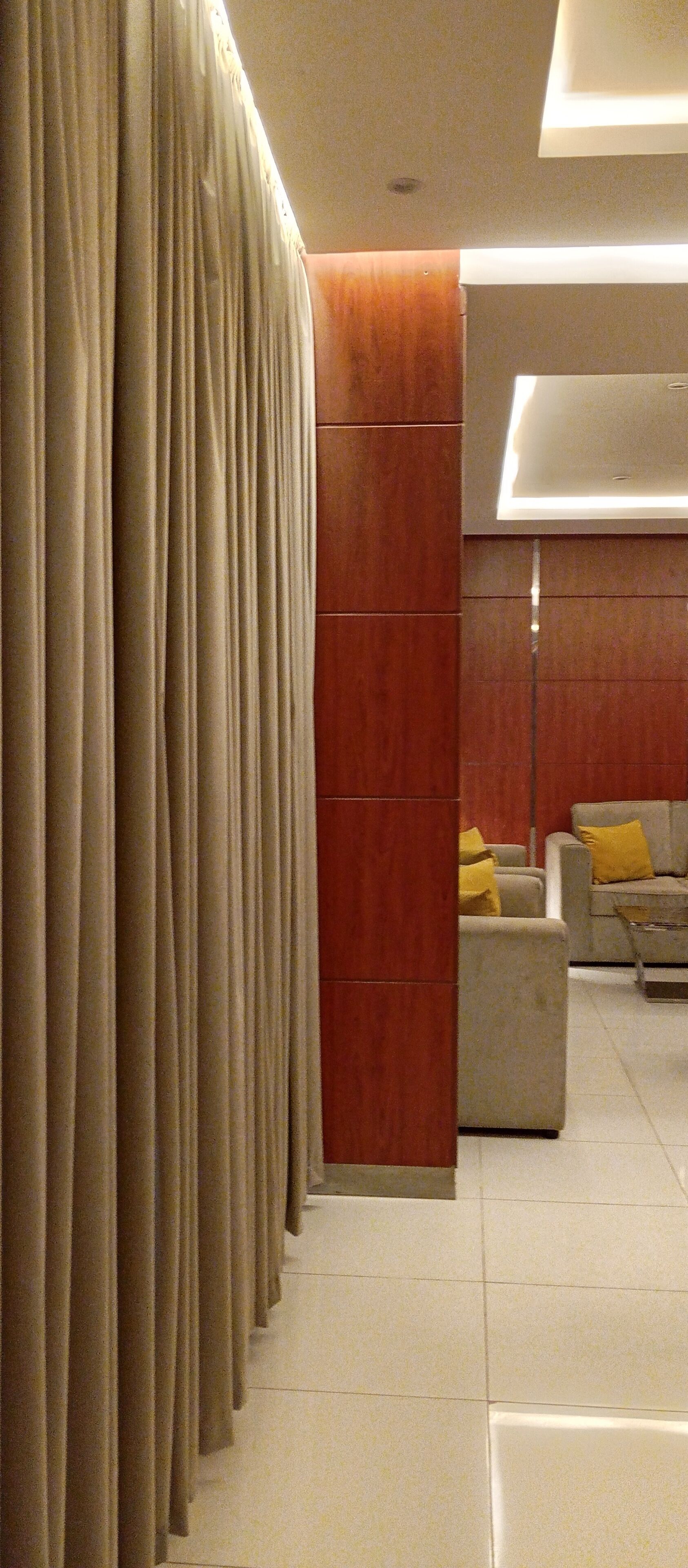 Un interior moderno con un separador de madera, un sofá con cojines amarillos y una zona cubierta por una cortina.