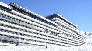 Een modern, meerlaags gebouw met een gebogen gevel, grote ramen en een besneeuwde omgeving.