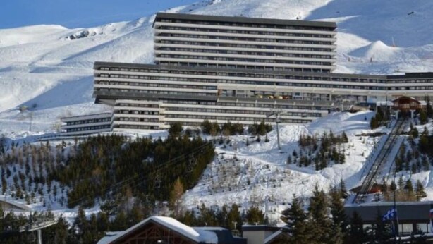 Een hotel met meerdere verdiepingen, een plat dak en een skilift op de achtergrond.