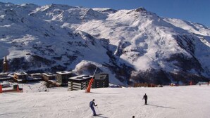 Een skigebied met besneeuwde hellingen, gebouwen en bergen op de achtergrond.