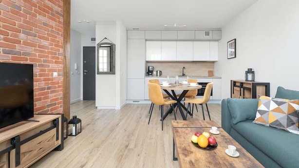 A modern living room with a brick accent wall, a television, and a dining area with a wooden table and chairs.