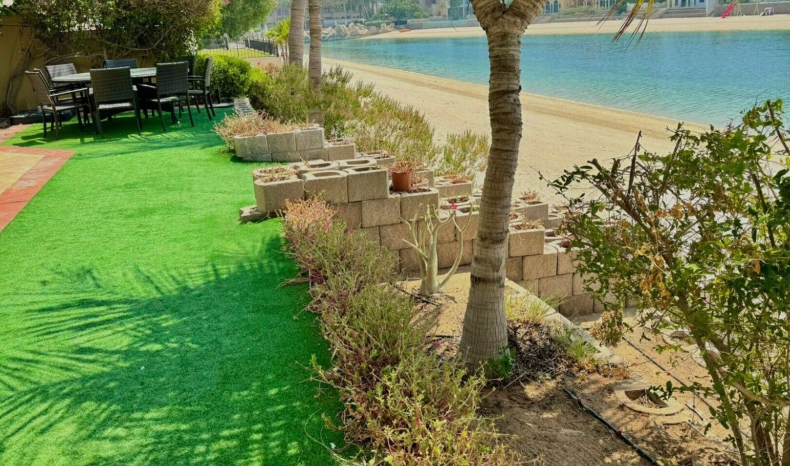 A poolside area with artificial grass, seating, and a view of the beach.