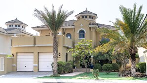 Una casa de dos pisos con fachada color beige, una torre central y un garaje.