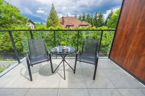 Ein Balkon mit rundem Tisch und zwei Stühlen, umgeben von einem Metallgeländer.