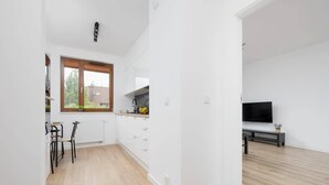 Una cocina moderna con armarios blancos, un comedor con dos sillas, un ventanal grande y un televisor de pantalla plana en la sala.