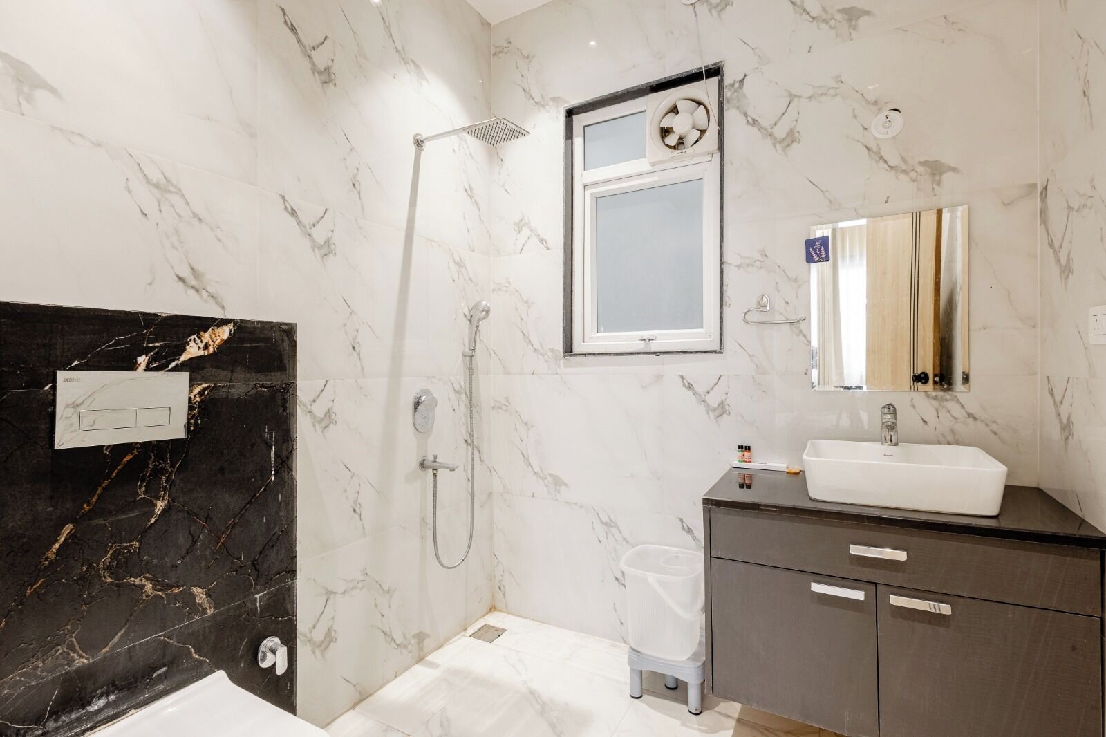 A bathroom with a black marble wall, a white sink, a mirror, and a shower with a handheld showerhead.
