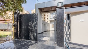 A modern building with a black metal gate, a paved entrance, and a clear view of the surrounding residential area. - Lime Tree B&B Pari Chowk (Greater Noida)