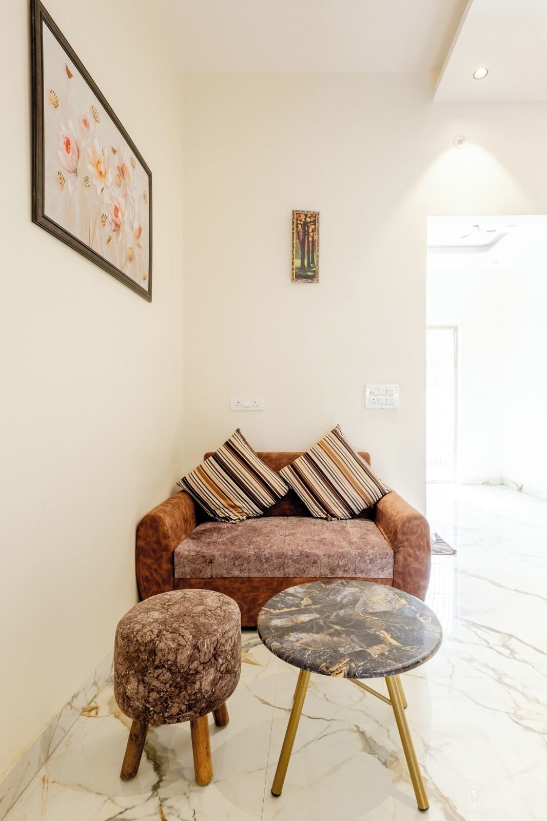 A living room with a sofa, two ottomans, a small round table, and two framed artworks on the wall.