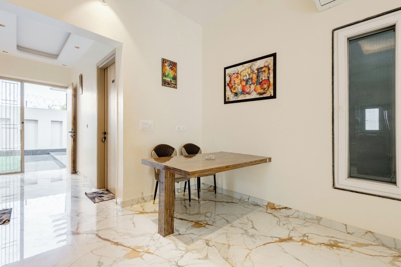 Un comedor con suelo de mármol, una mesa de madera y dos sillas. Hay dos obras de arte enmarcadas en la pared.