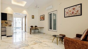 A spacious living area with a marble floor, a dining table with chairs, a sofa, and artwork on the walls. - Lime Tree B&B Pari Chowk (Greater Noida)