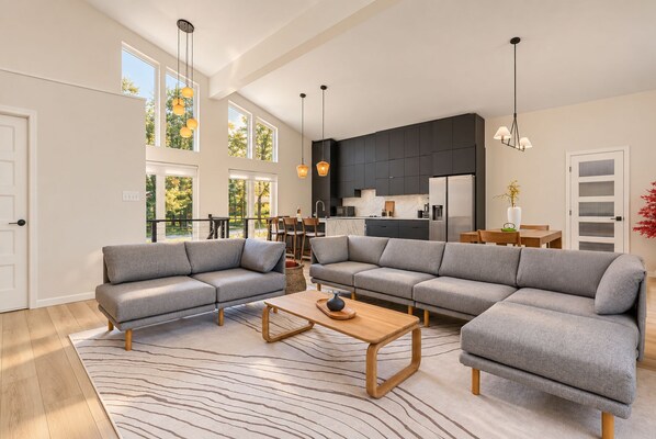 A modern living room with a sectional sofa, a coffee table, and a dining area with a kitchen in the background.