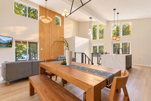 A modern interior with a wooden dining table, grey sofa, and a kitchen area with a marble countertop.