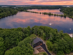 A large body of water surrounded by dense forest, with a single building featuring a sloped roof and a visible driveway. - Autumn Lakefront: Natural Hot Tub: Private Dock: Play Area (Pocono Summit)