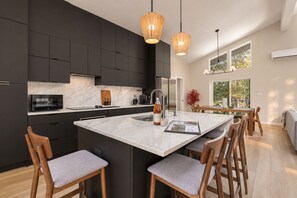 A modern kitchen with dark cabinetry, a large island, and wooden bar stools.