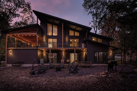 A modern two-story house with a covered patio area, outdoor seating, and a grill.