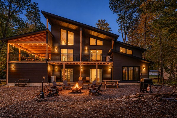 A modern two-story house with a covered patio, outdoor seating, and a fire pit.