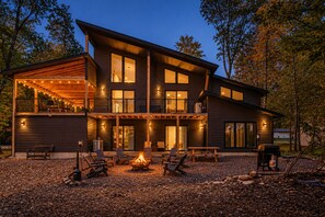 A modern two-story house with a covered patio, outdoor seating, and a fire pit.