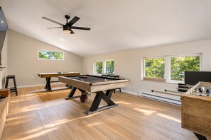 A pool table in a room with wooden flooring, a ceiling fan, and windows with a view of greenery. - Autumn Lakefront: Natural Hot Tub: Private Dock: Play Area (Pocono Summit)