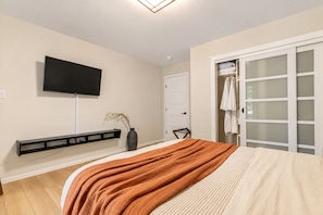 A bedroom with a bed, a TV mounted on the wall, a wardrobe with frosted glass doors, and a small shelf with a vase. - Autumn Lakefront: Natural Hot Tub: Private Dock: Play Area (Pocono Summit)
