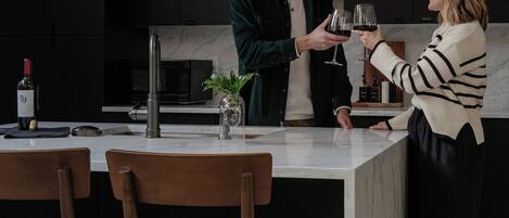 Una cocina moderna con armarios oscuros, una encimera de mármol y dos lámparas colgantes.