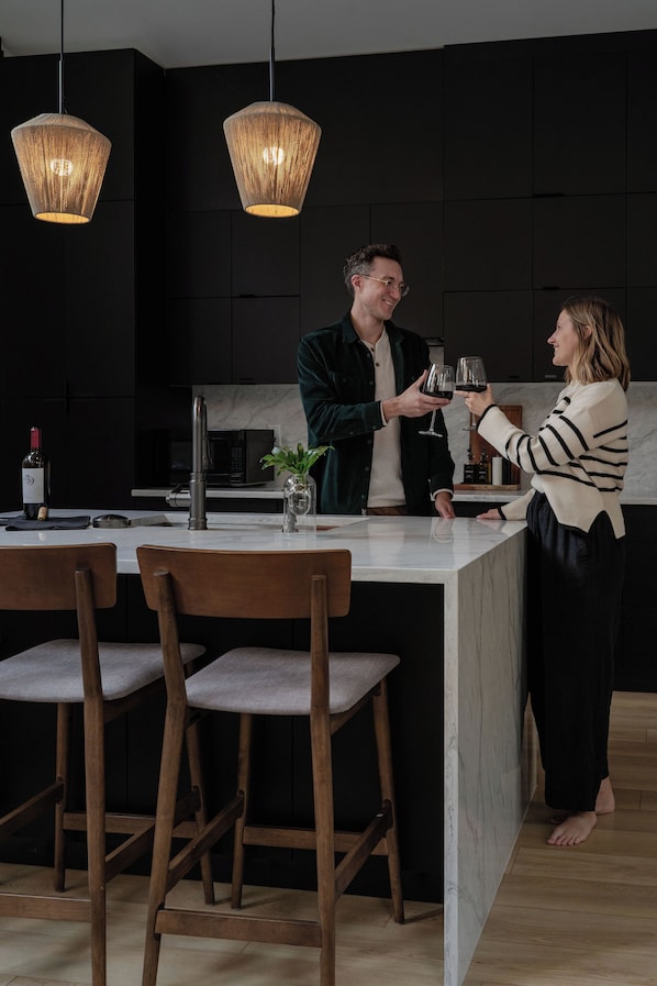 A modern kitchen with dark cabinetry, a marble countertop, and two hanging pendant lights.