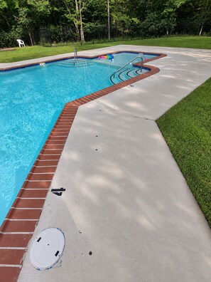 A swimming pool with a brick border and a concrete deck.