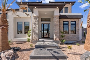 A modern two-story house with a stone facade, large windows, and a central entrance. - Pecan Valley Oasis | Lux Pool & Family Retreat (Hurricane)