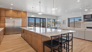 Una cocina moderna con armarios de madera, un refrigerador de acero inoxidable, una isla grande con taburetes de bar y un ventanal con vistas al paisaje.