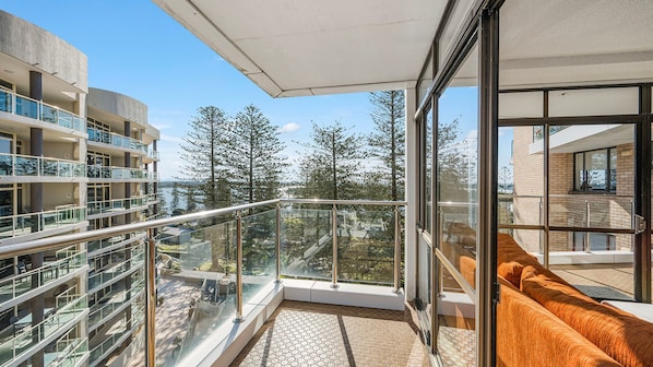 A balcony with glass railings overlooking a residential area and trees.