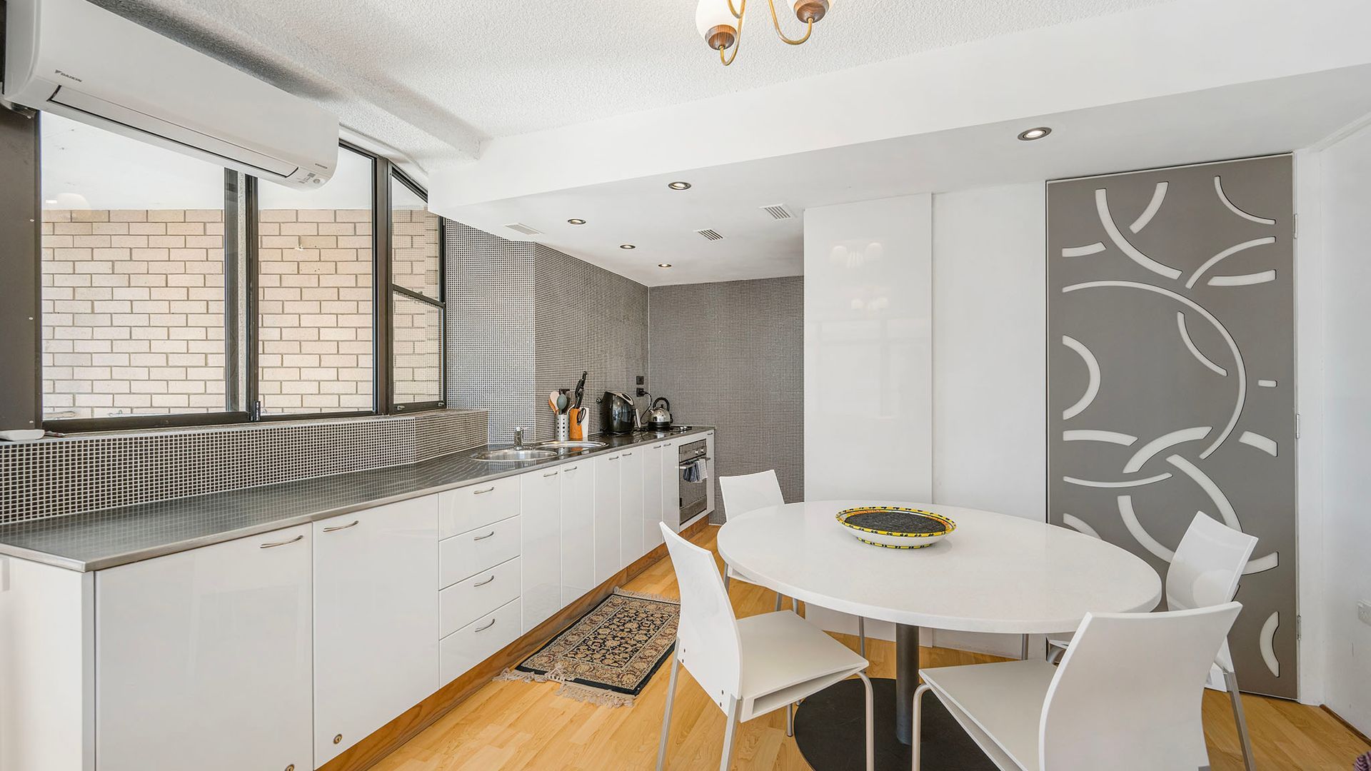 A modern kitchen with white cabinetry, a built-in oven, and a dining area with a round table and chairs.