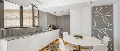 A modern kitchen with white cabinetry, a built-in oven, and a dining area with a round table and chairs.