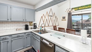 A kitchen with grey cabinets, a white countertop, a coffee maker, and a view of the mountains through the window.