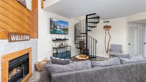 A modern living room with a fireplace, a sofa, a coffee table, and a spiral staircase.